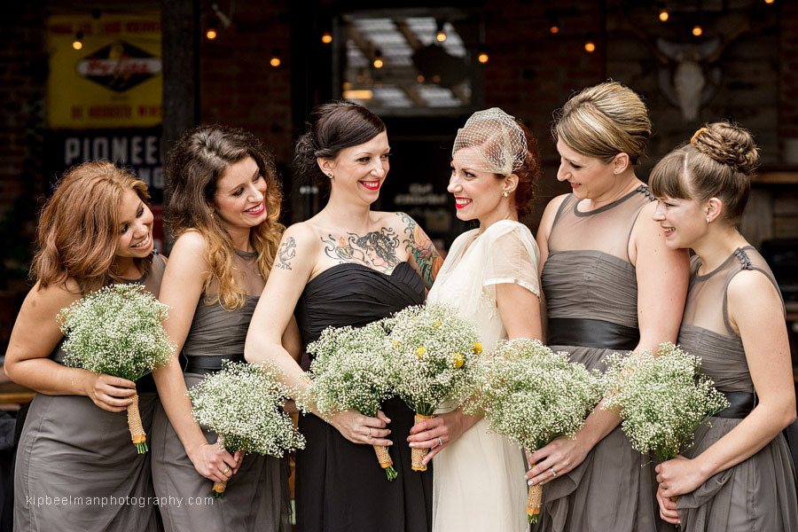 A bride and her bridesmaids interact casually with big smiles on the patio of King's Hardware in Ballard before their Golden Gardens Bathhouse wedding