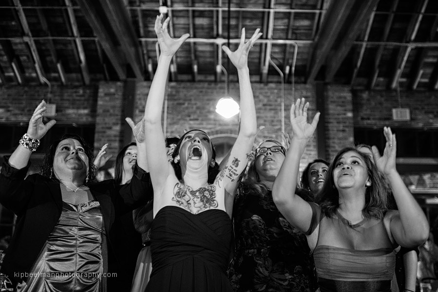 Mouths are agape and arms outstretched in an effort to catch the tossed bouquet at a Golden Gardens Bathhouse Wedding