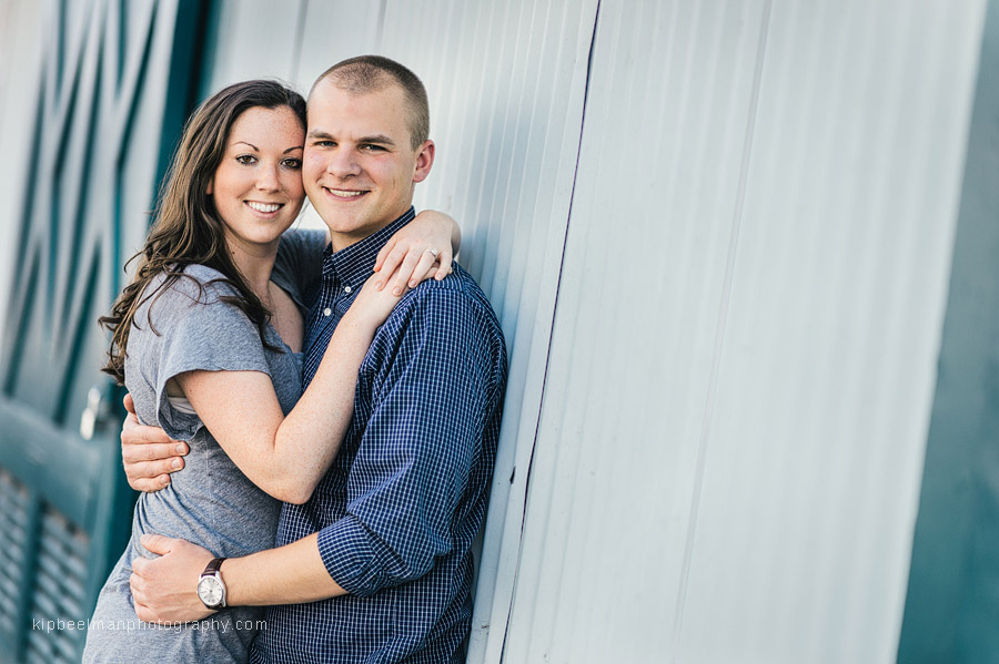 A Fishermens Terminal engagement session sees a couple posing together against a net shed wall