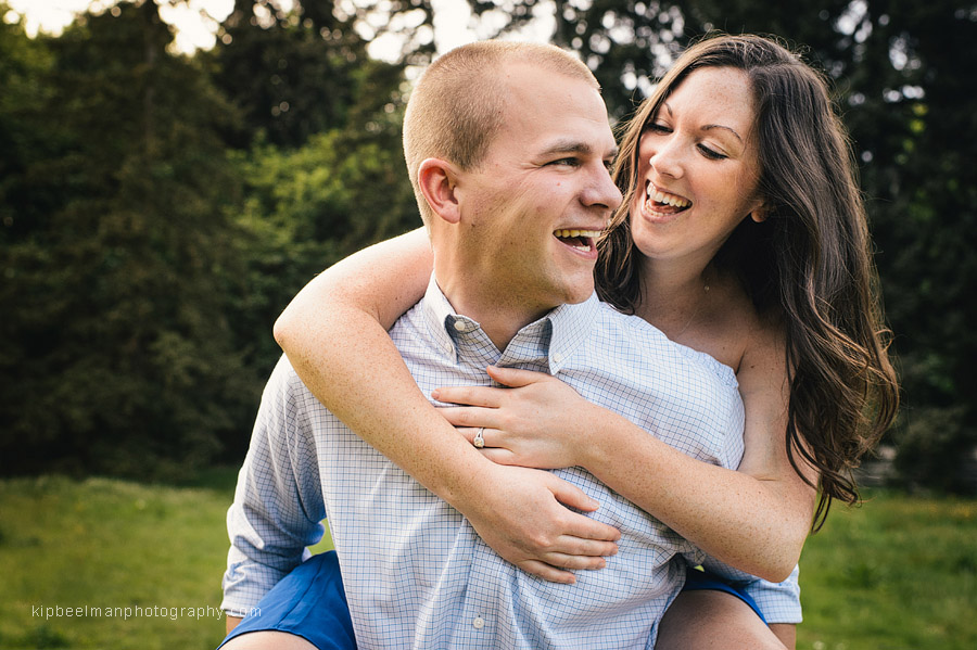 A smiling guy give a smiling girl a piggy back ride in Discovery Park after their Fishermens Terminal engagement session